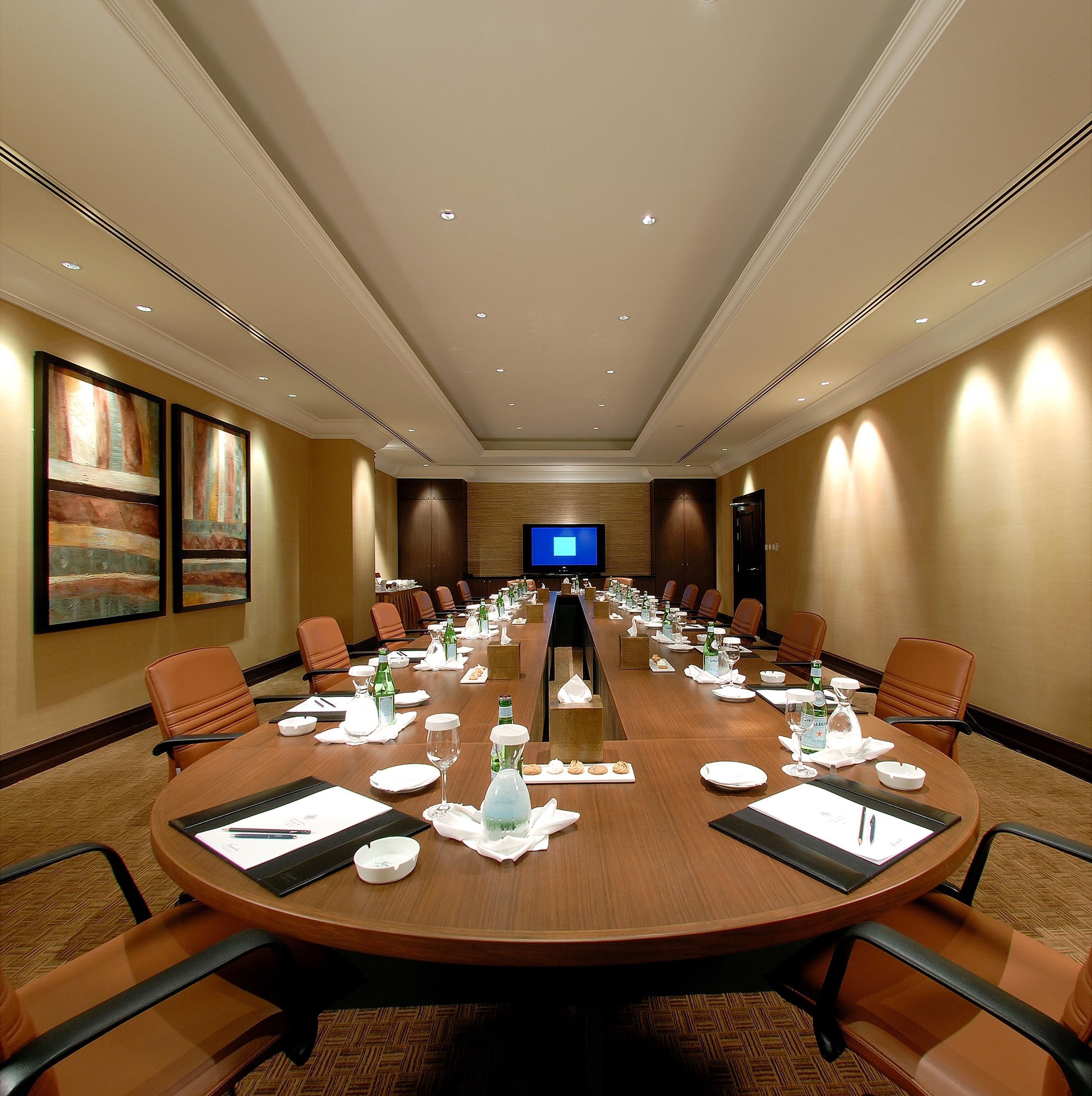 A conference room with a long table, chairs, and a television screen.