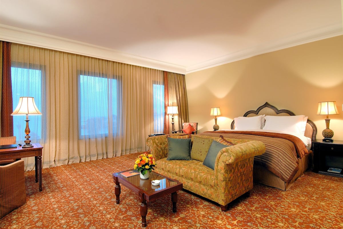 A hotel room with a bed, sofa, armchair, and a coffee table with flowers.