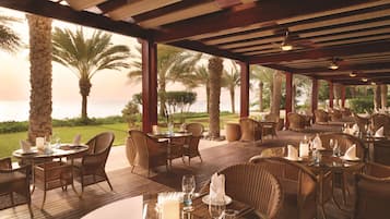 Un espace de restauration en plein air avec des tables et des chaises, des palmiers et une vue sur la mer.