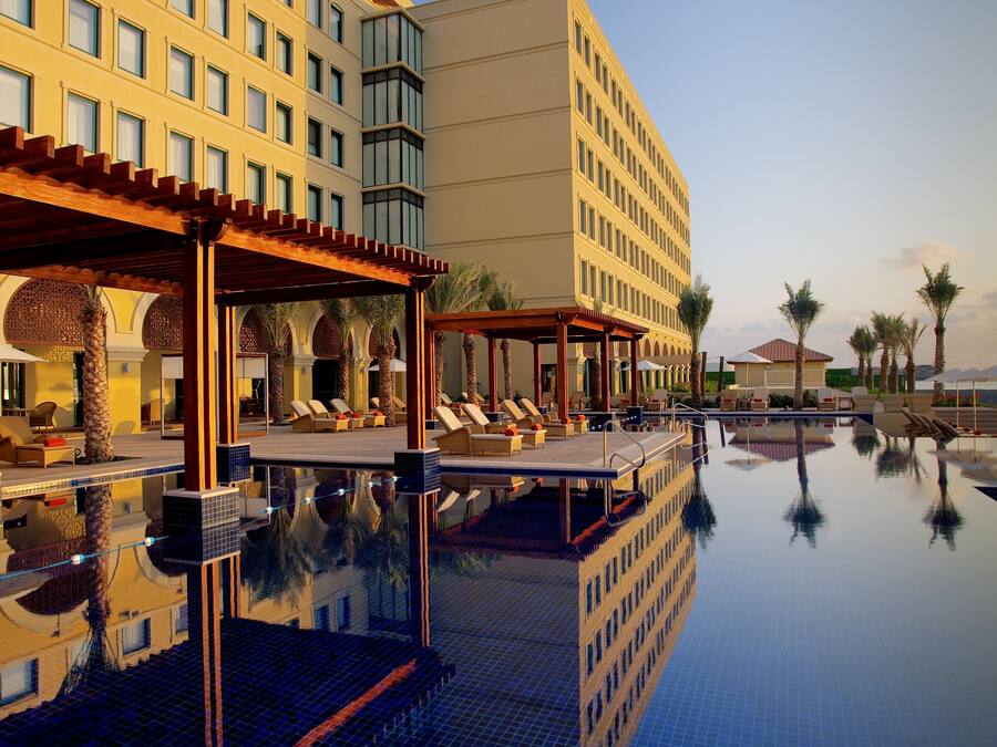 Un hotel con piscina, sillones de descanso y palmeras.