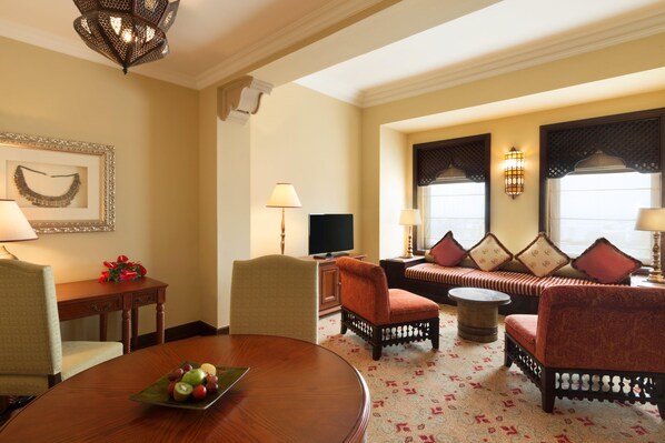 A well-lit living room with a round wooden table, comfortable seating, a television, and decorative wall sconces.