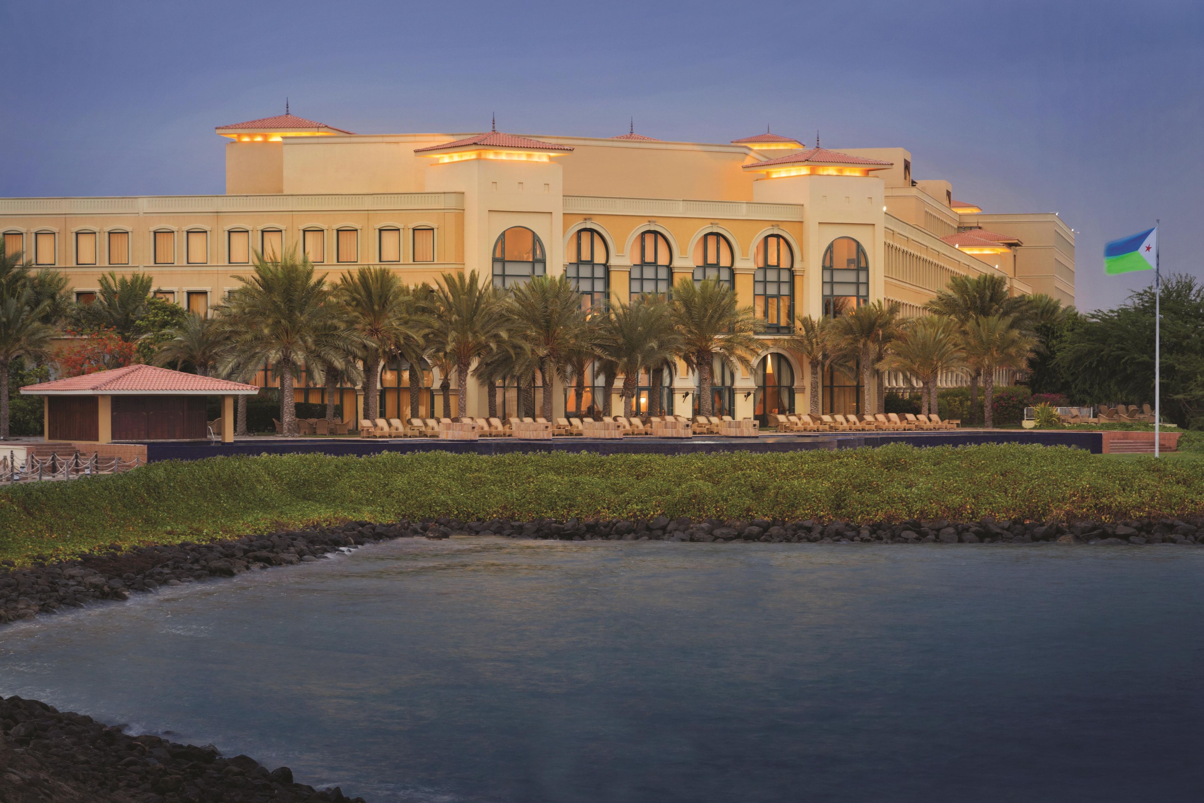 A large hotel with multiple floors, a swimming pool, and palm trees.