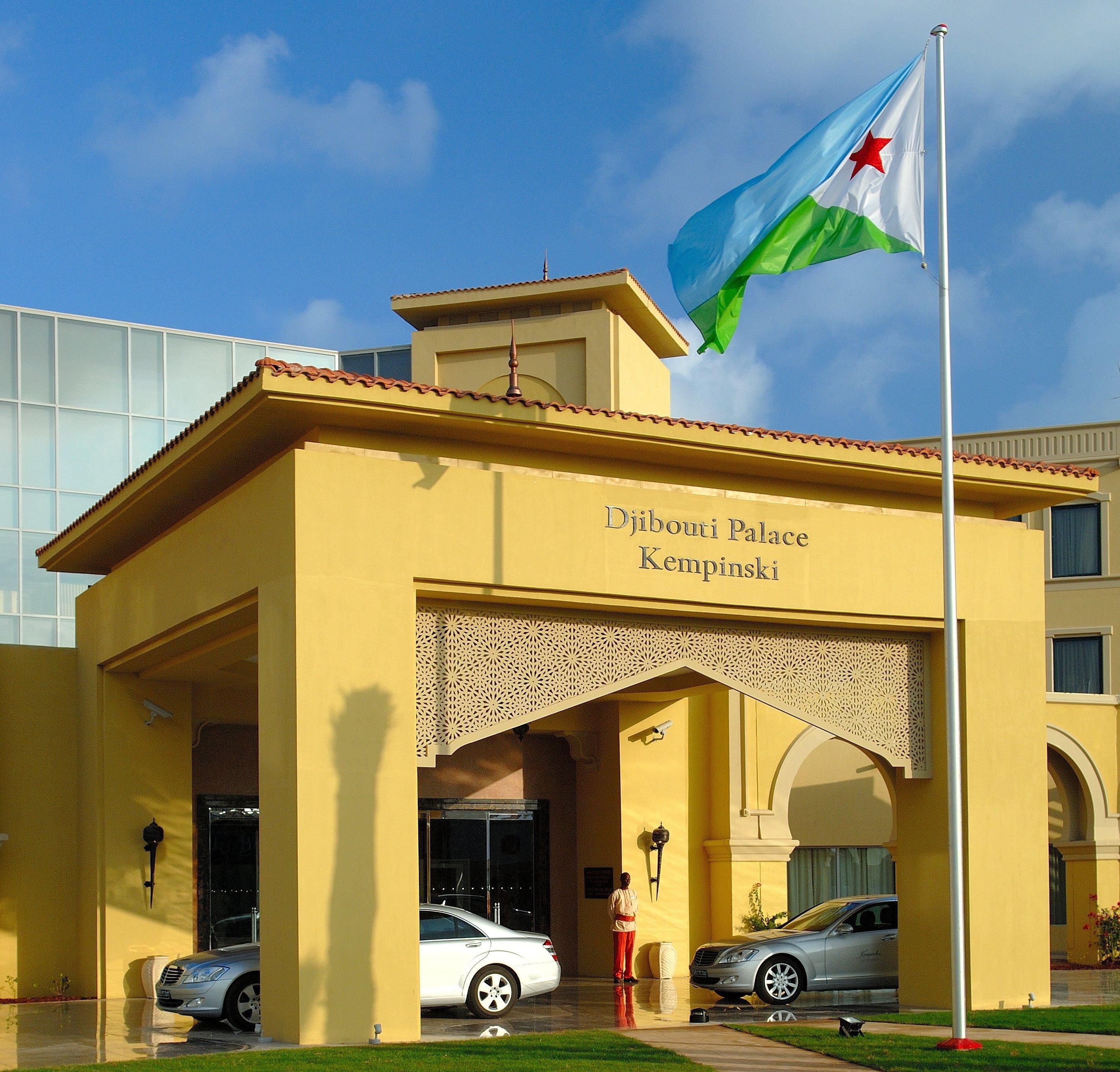 Djibouti Palace Kempinski with a flag, two cars, and a person standing in front.