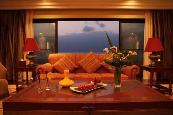 A living room with a sofa, a coffee table with decorative items, and a view of the outdoors through large windows. - Djibouti Palace Kempinski (Djibouti)