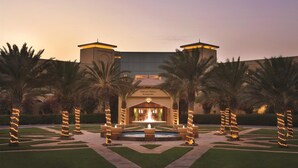 En väl upplyst entré med en fontän, palmer och en byggnad med skylten ”Djibouti Palace Kempinski”.