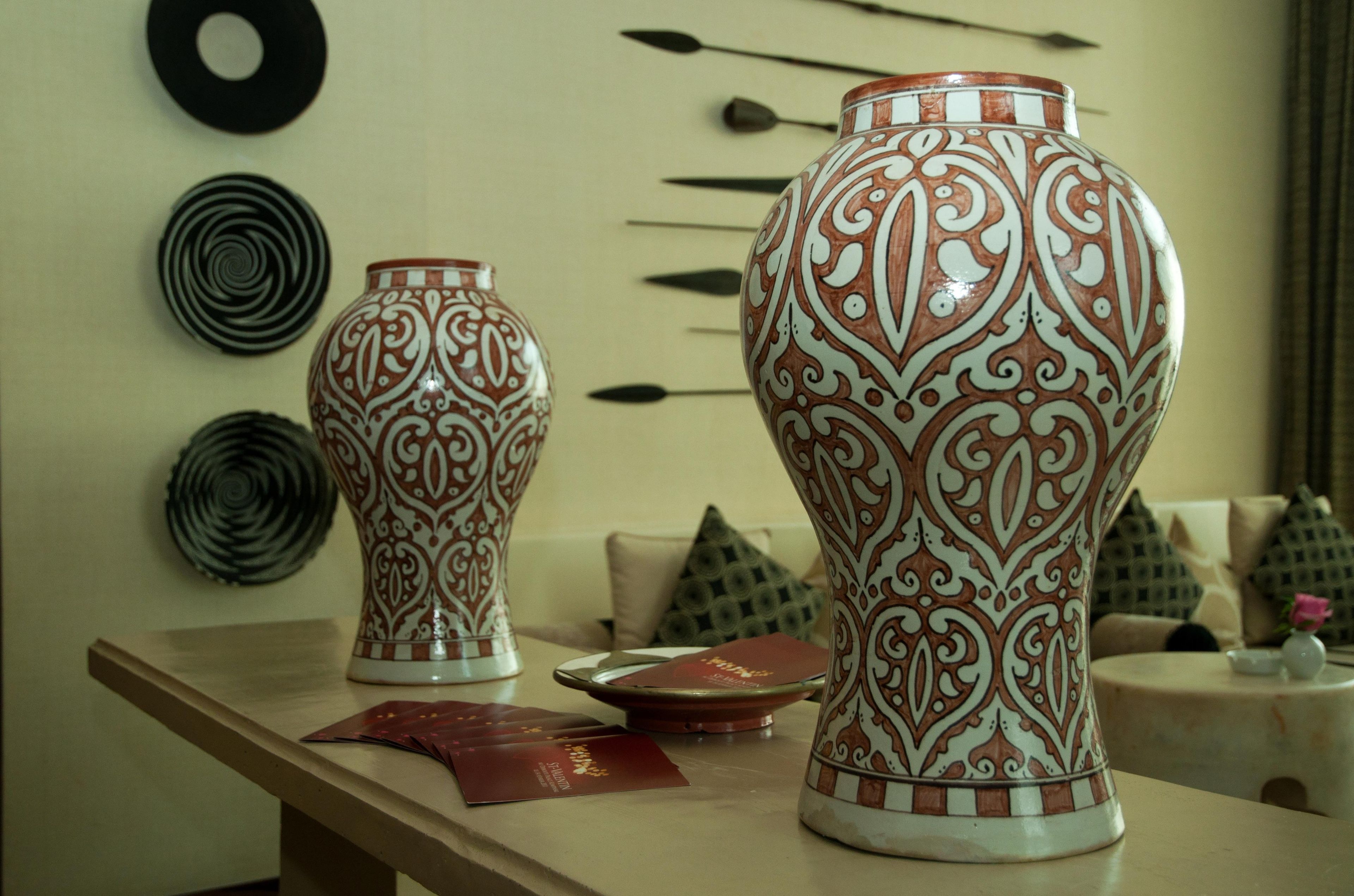 Dos jarrones decorativos sobre una mesa, con adornos de pared con motivos en el fondo.