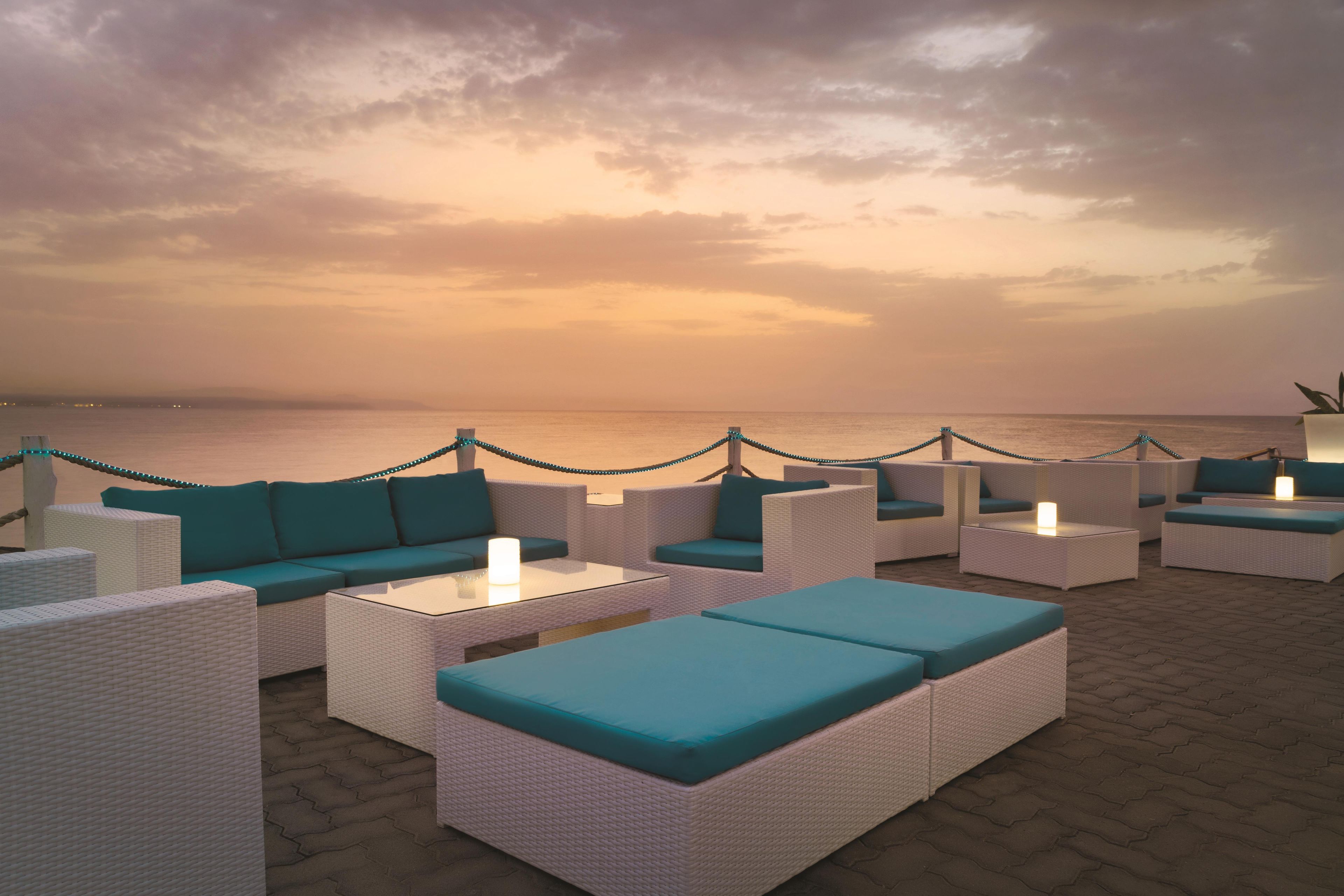 An outdoor seating area with wicker furniture and teal cushions, overlooking a body of water.