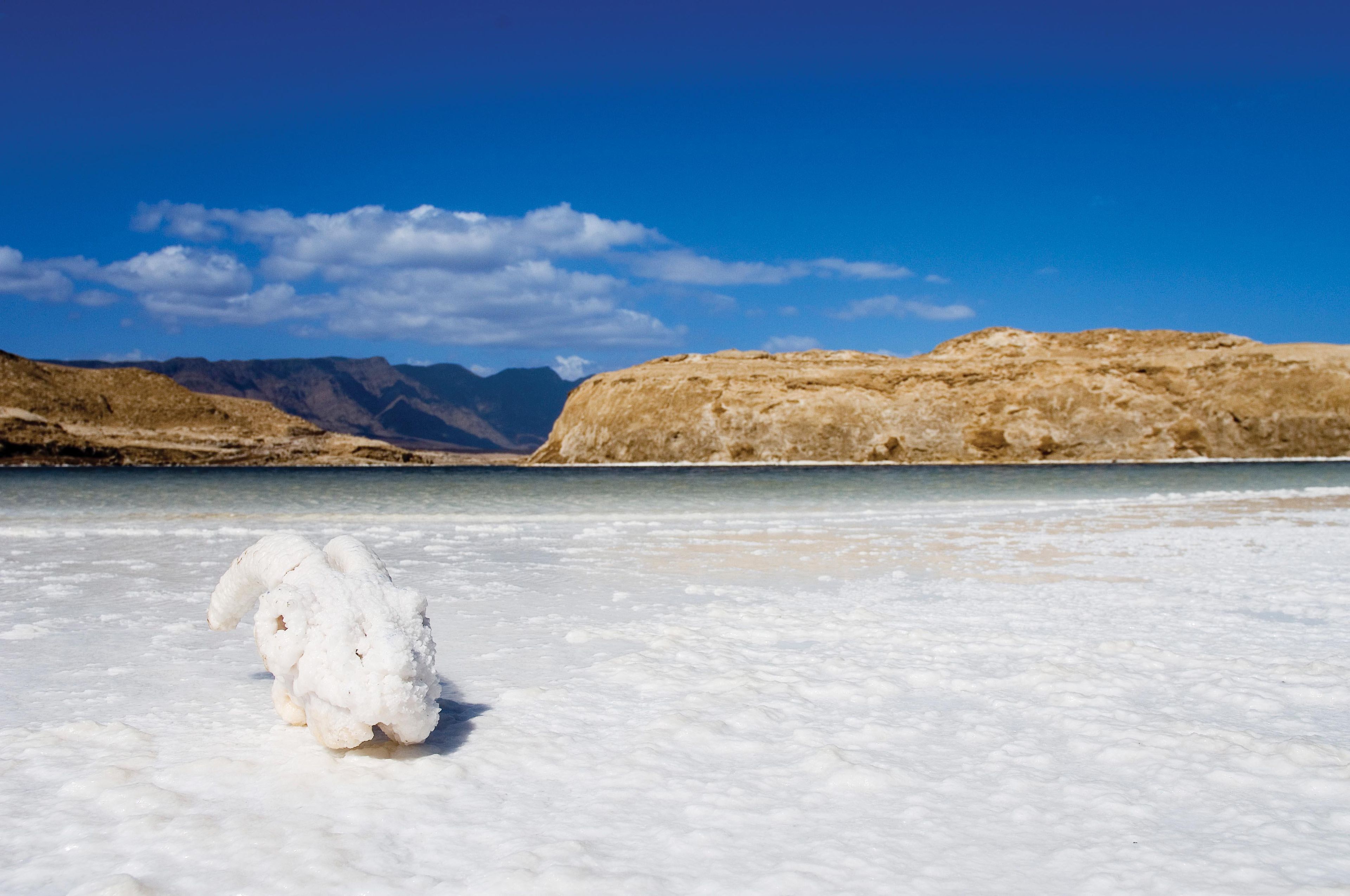 A salt flat with a large salt formation in the foreground and mountains in the background.