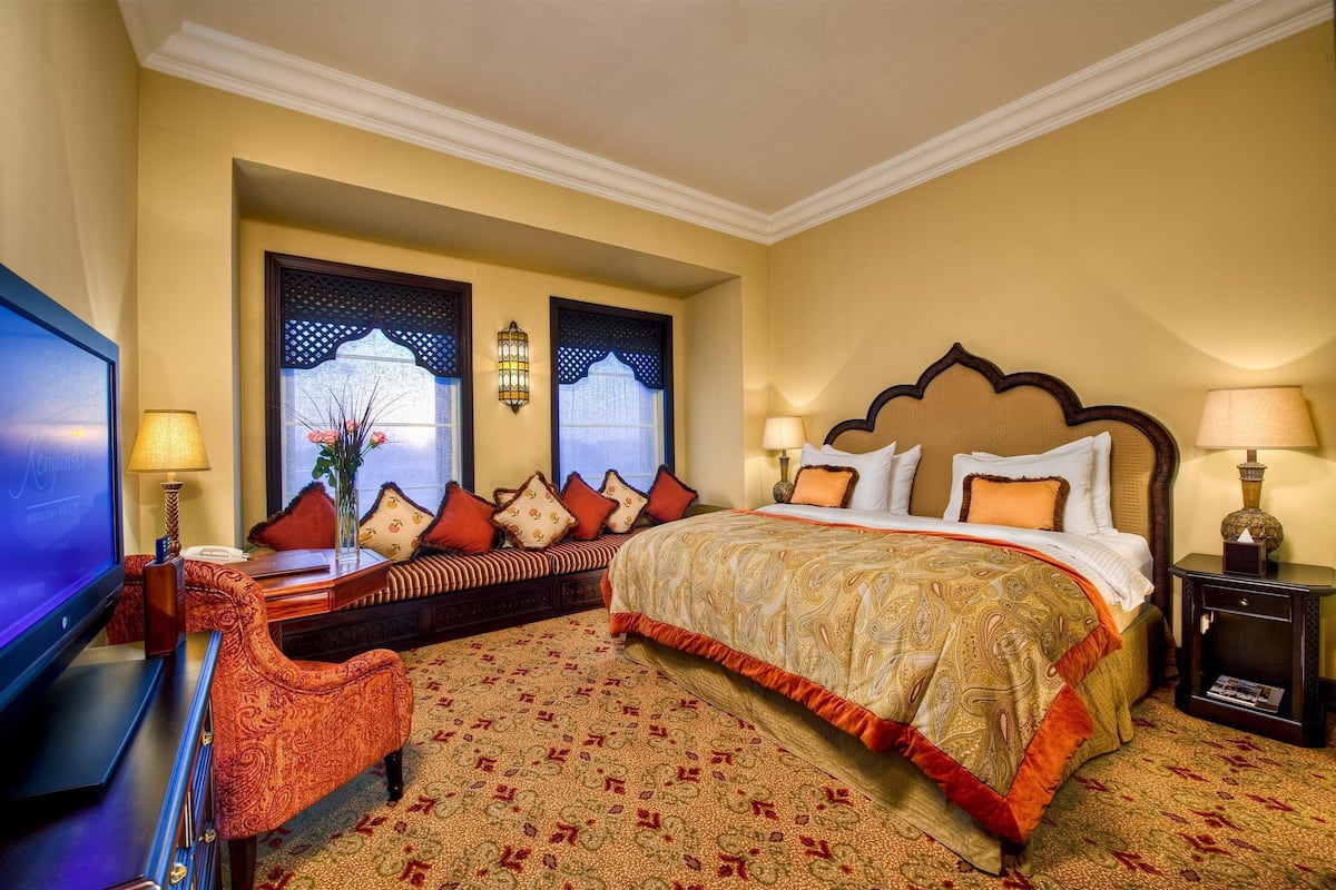A hotel room with a large bed, a television, a sofa, and a desk with a lamp.