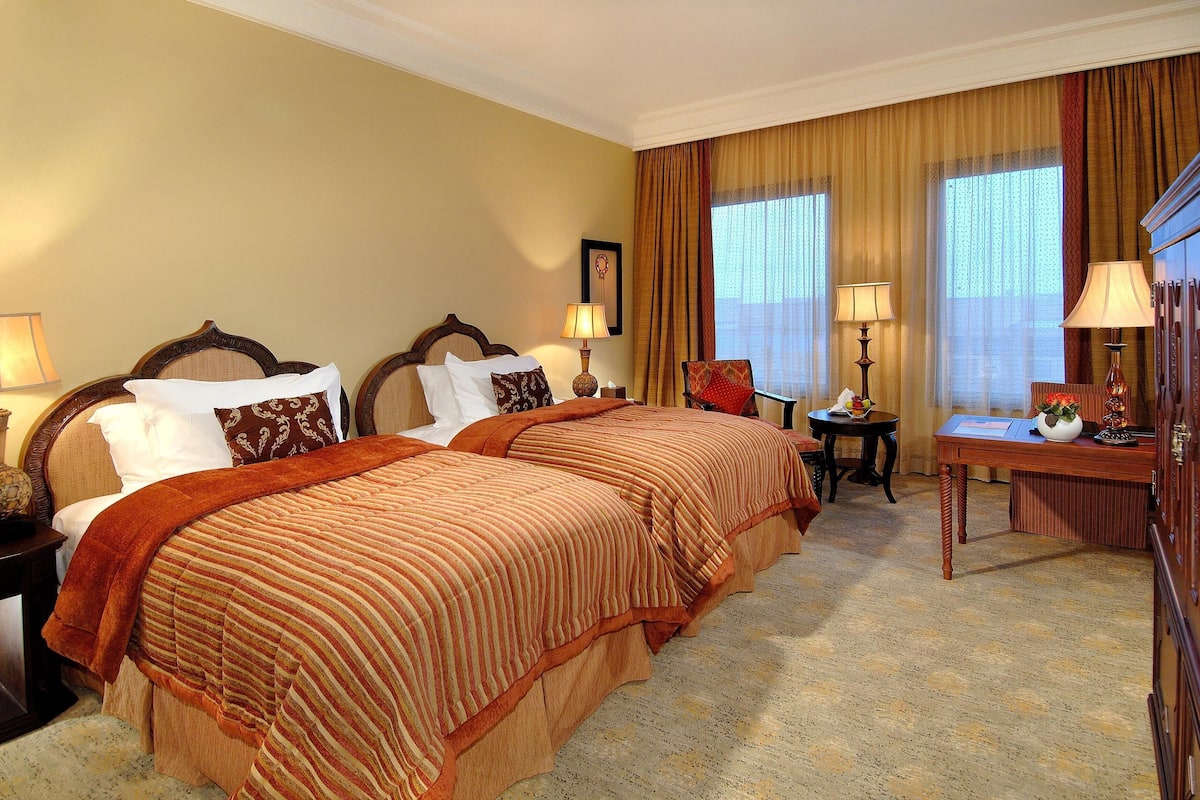 A hotel room with two beds, a desk, and a chair.