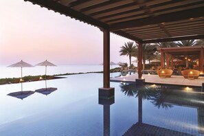 Ein ruhiger Infinity-Pool mit Blick auf das Meer, umgeben von Liegestühlen und Sonnenschirmen.