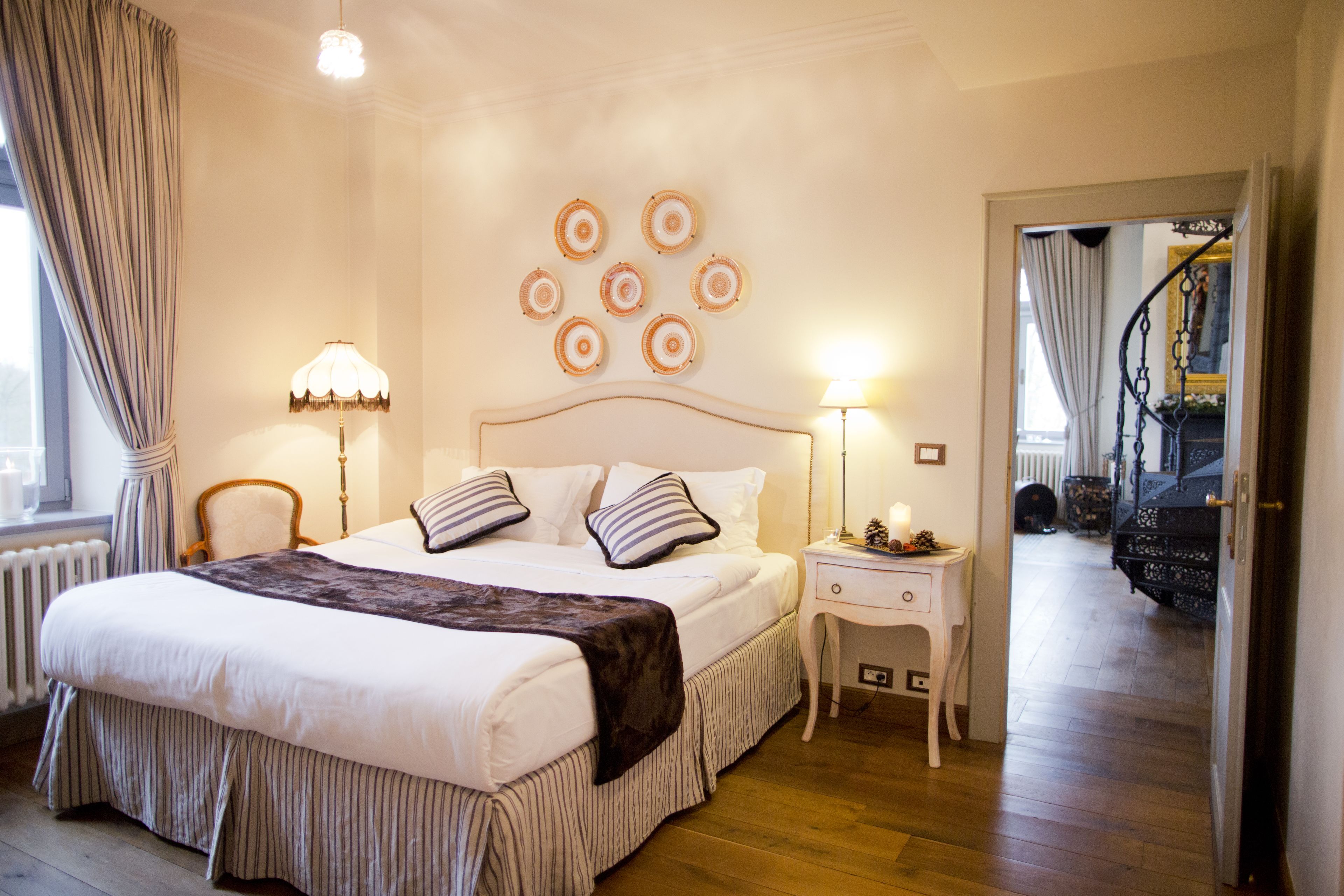 A bedroom with a large bed, two bedside tables with lamps, a chair, and a wall with circular decorations.