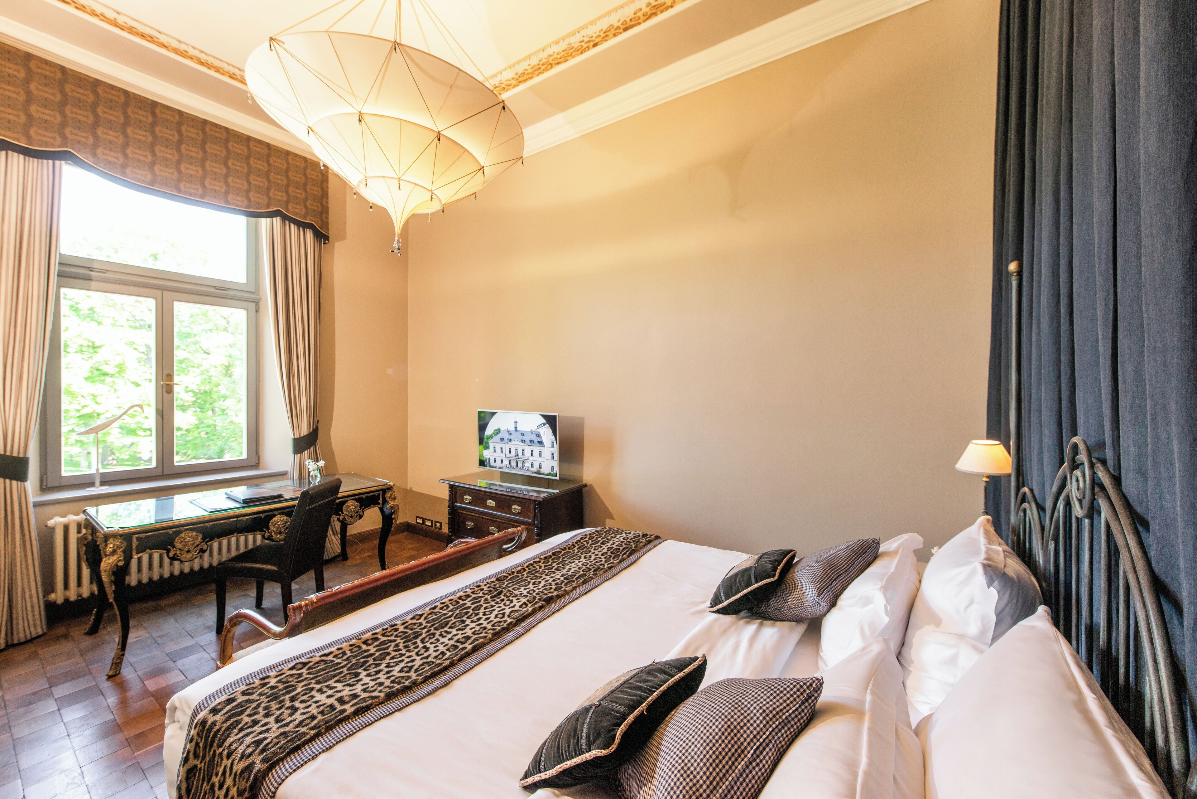 A hotel room with a large bed, a desk with a chair, a television, and a window with curtains.