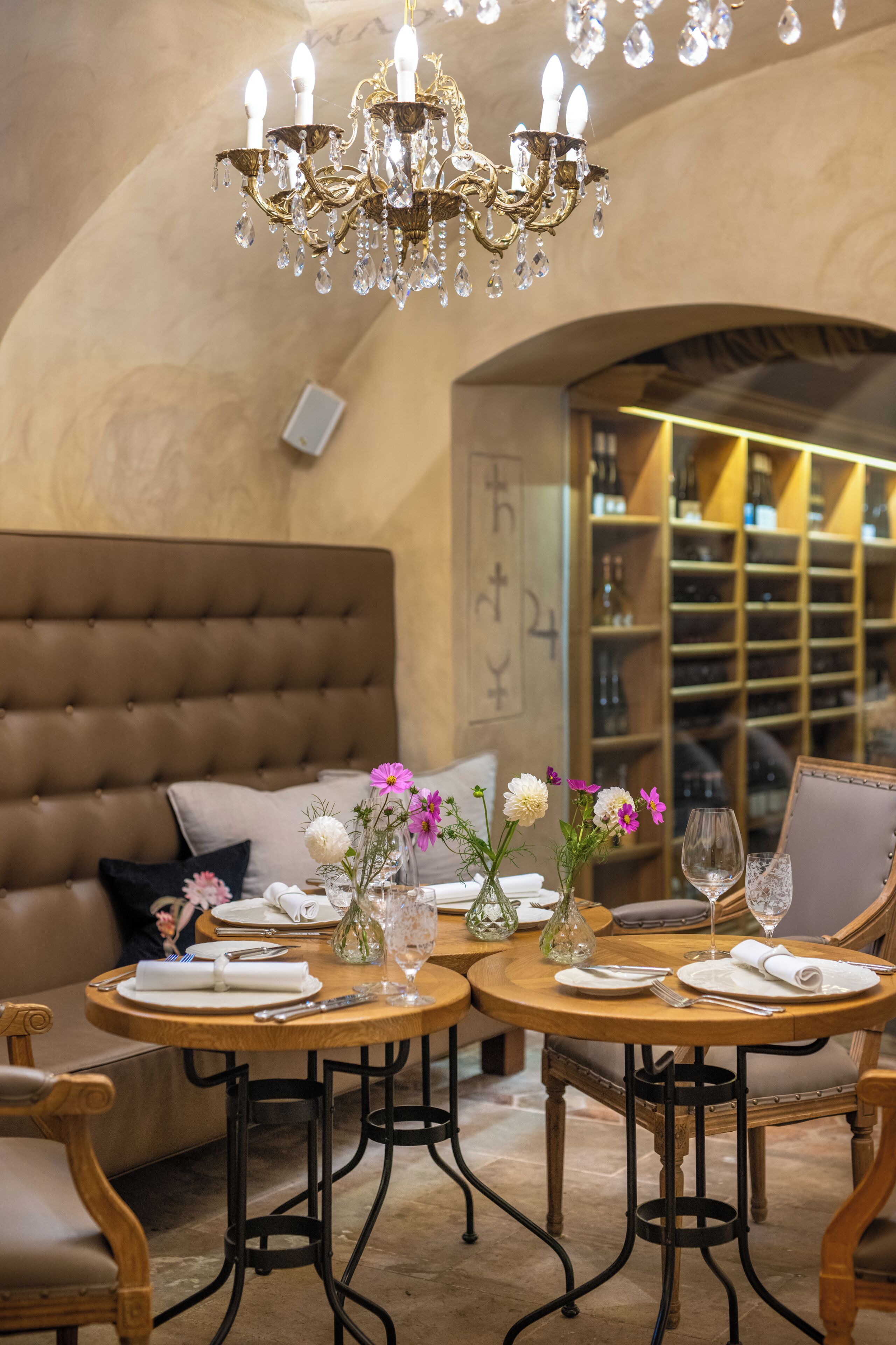 Un espace repas agrémenté d’un lustre, de tables rondes et d’un meuble à vin en arrière-plan.