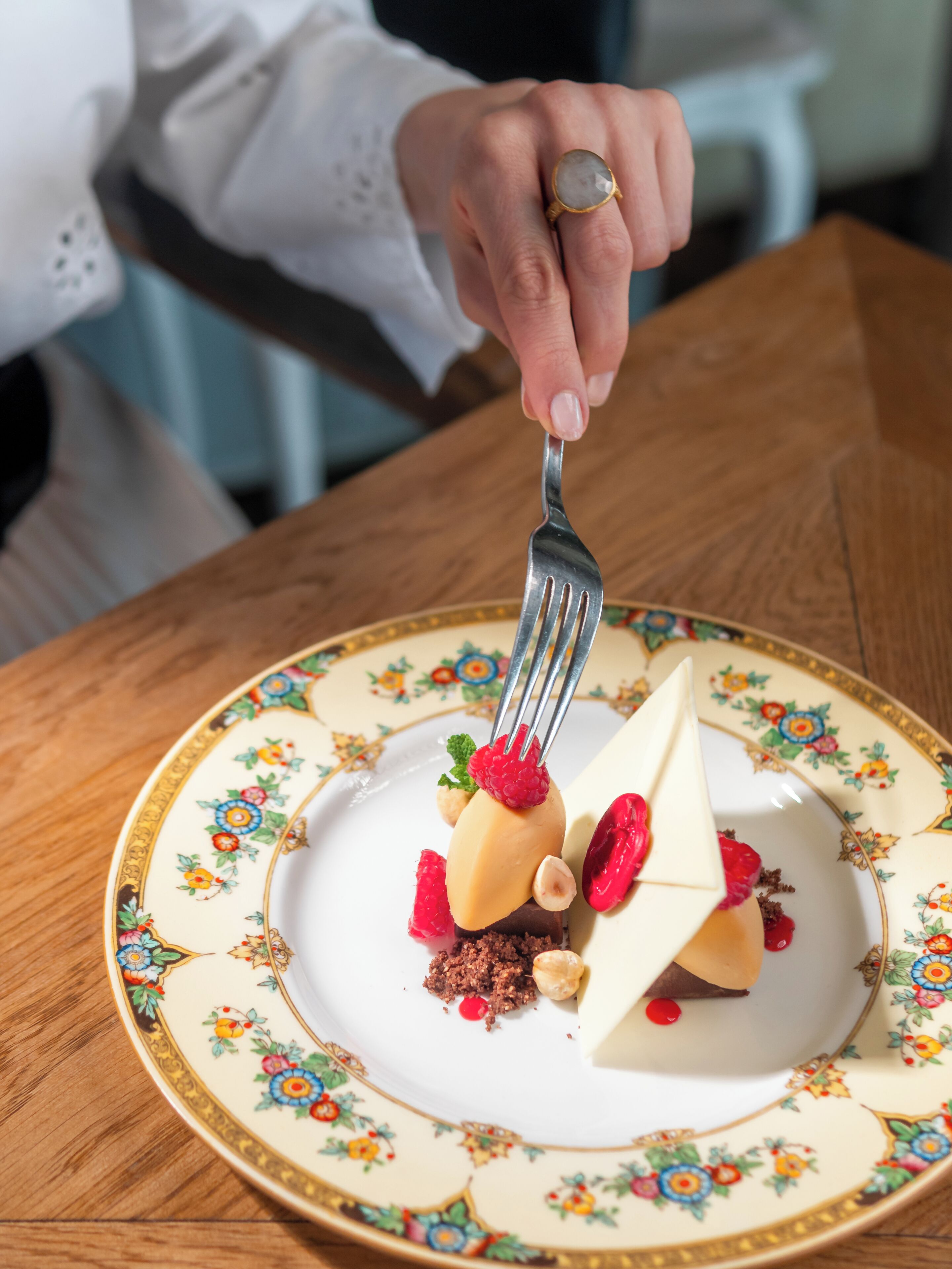 A person holding a fork over a dessert on a floral plate.