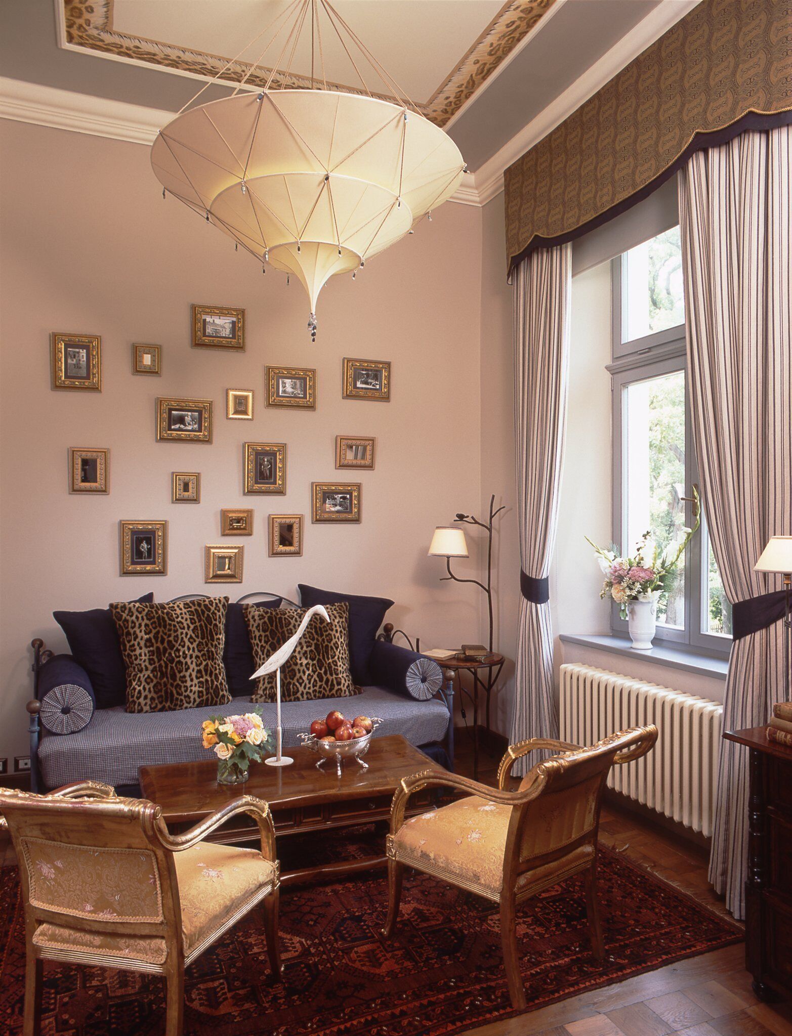 Una habitación con sofá, sillas, una mesa con flores, cuadros en la pared y una ventana con cortinas.