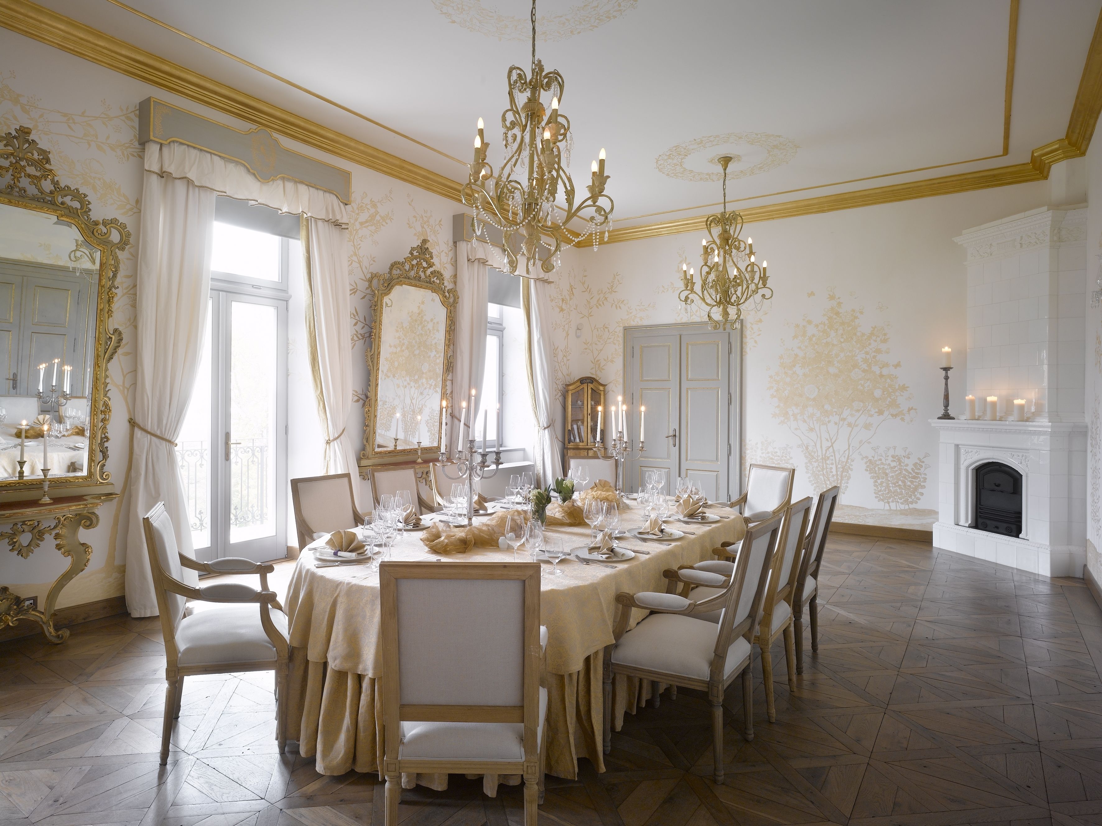 A formal dining room with a large table set for a meal, elegant chandeliers, and a fireplace.