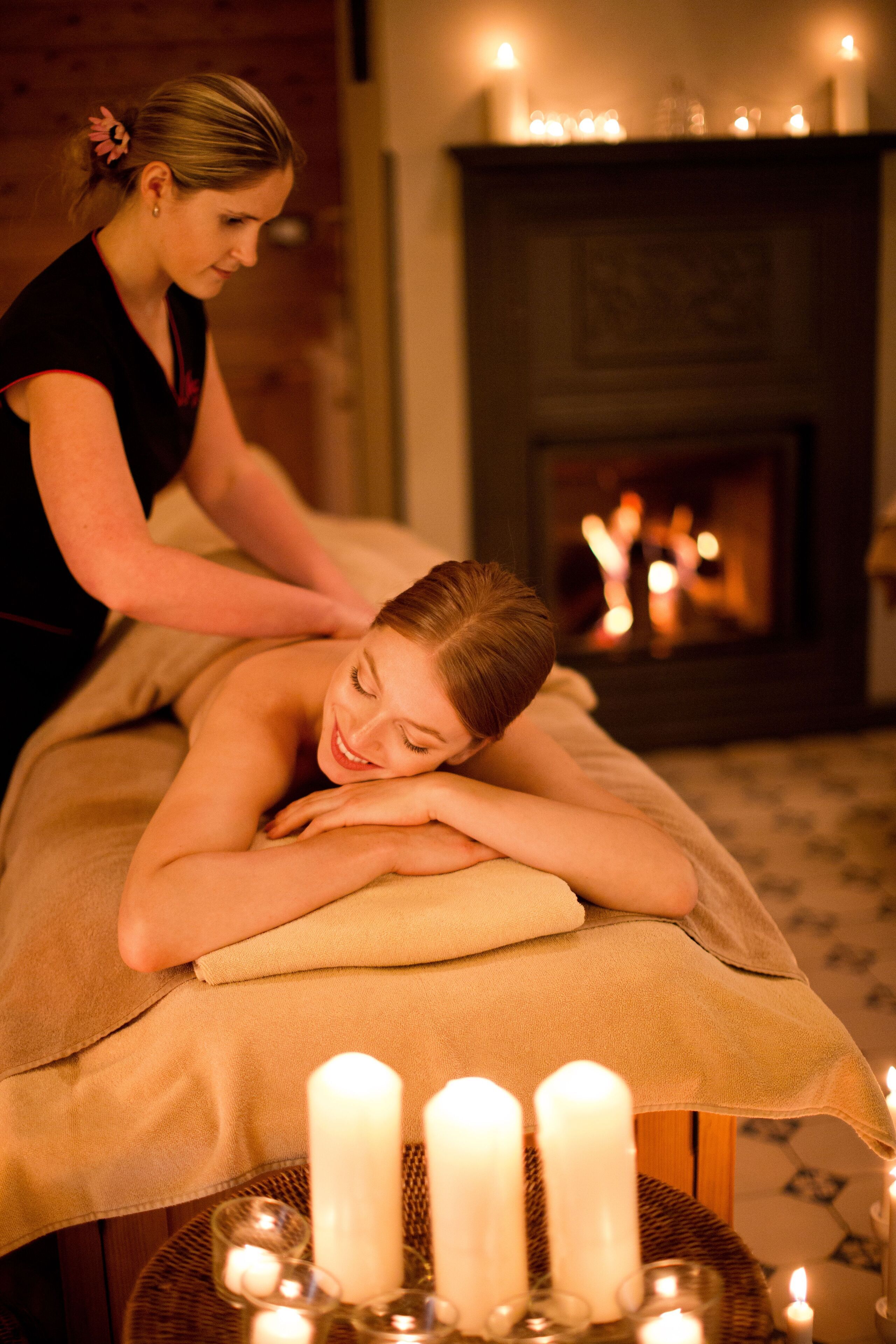 A massage therapy session in a room with a fireplace and candles.