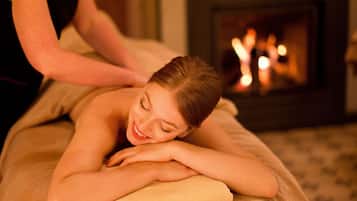 A massage therapy session in a room with a fireplace and candles.