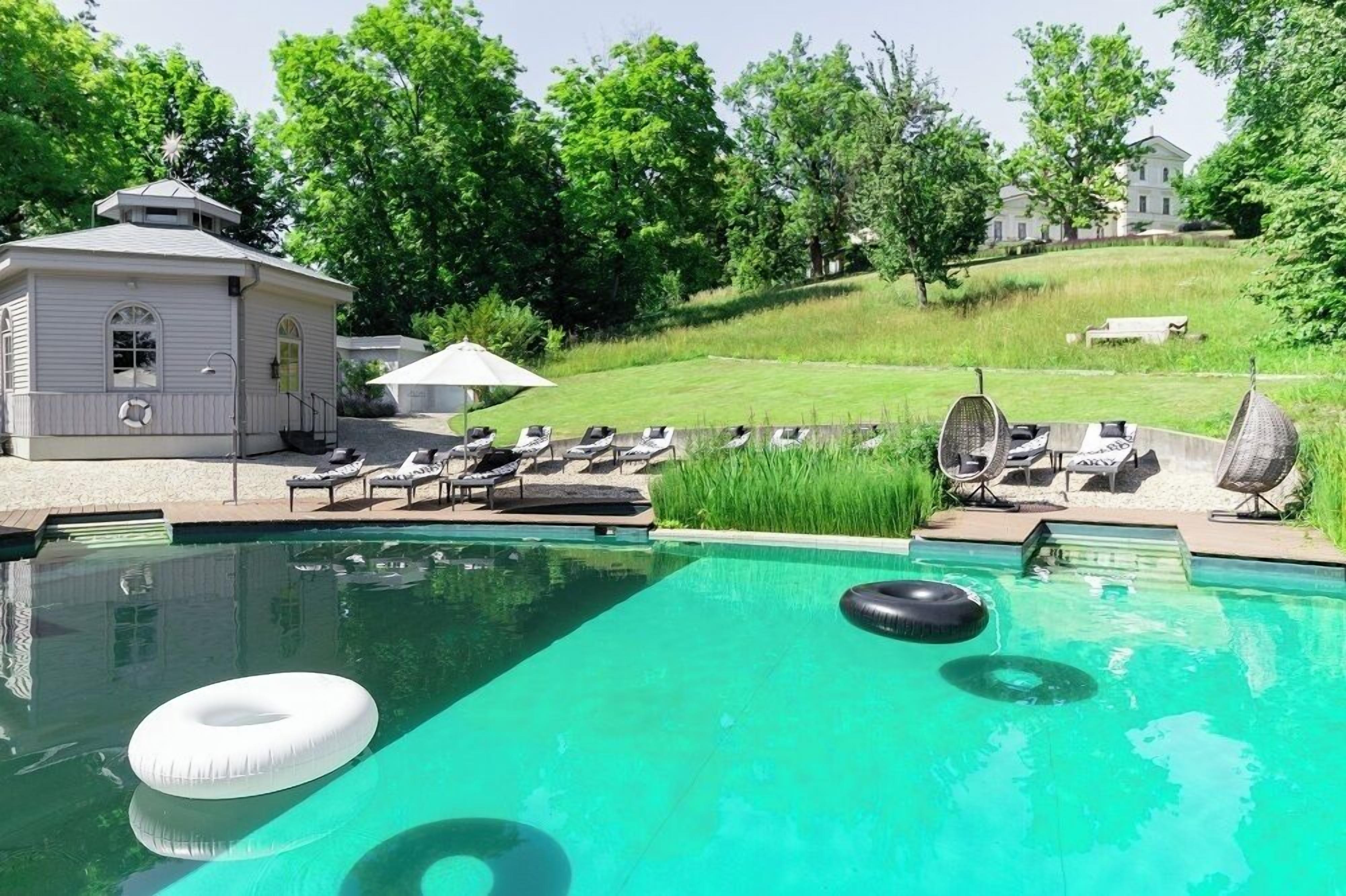 Una piscina con sillas de descanso y un edificio pequeño, rodeado de vegetación y una colina.