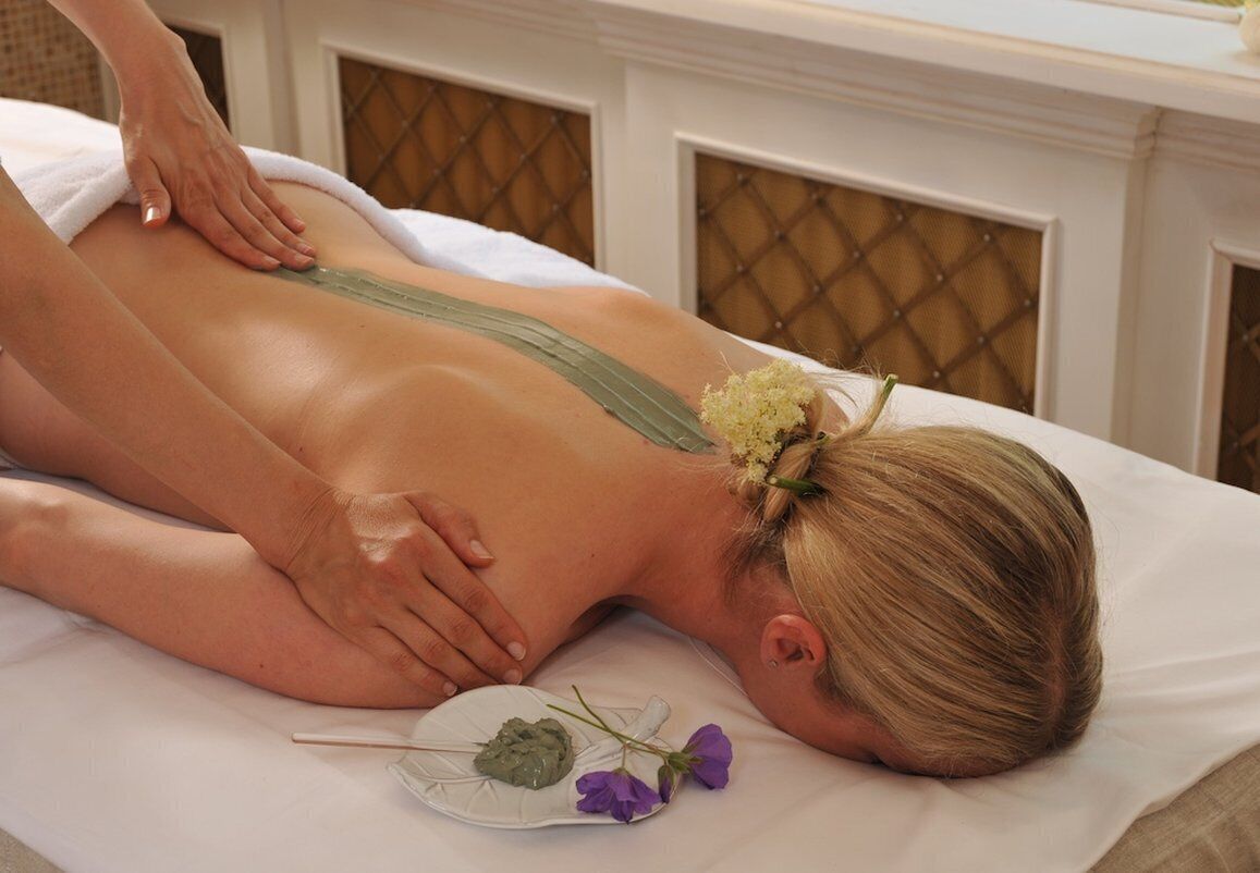 En person får en massage på ryggen i ett rum med en vit säng och en dekorativ sänggavel.
