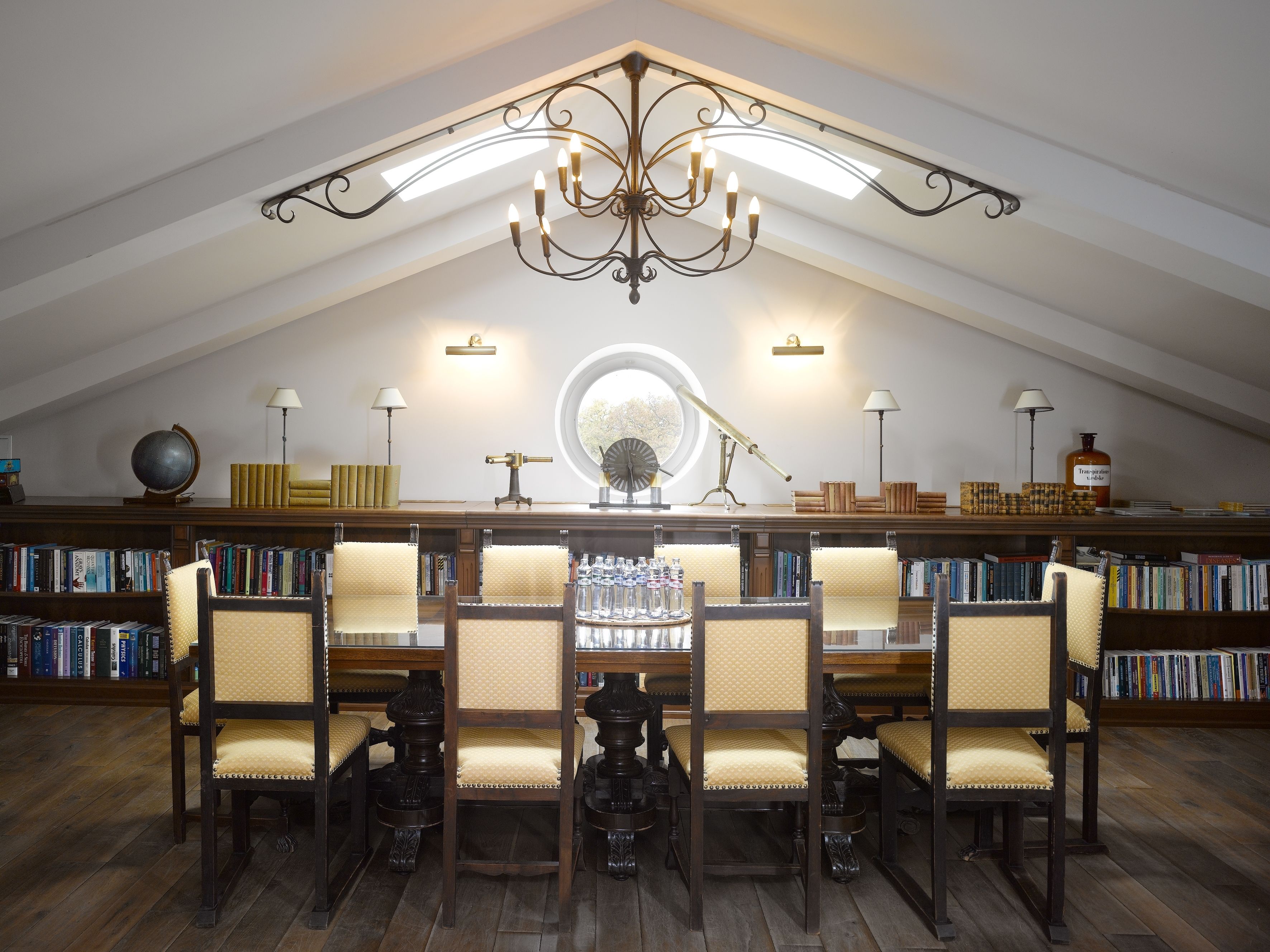 A library with a high ceiling, bookshelves, a round table, and six chairs.
