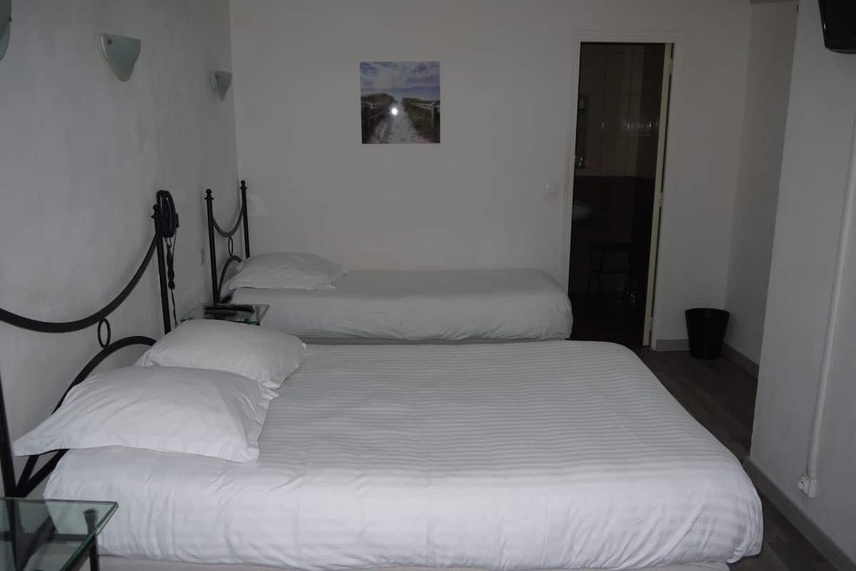 A bedroom with two single beds, a small bedside table, a wall-mounted lamp, and a picture on the wall.