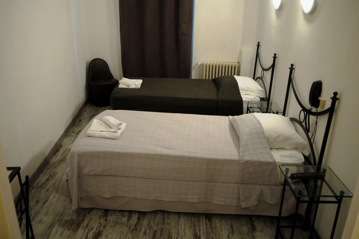 A small, compact room with two single beds, a small table, and a chair.