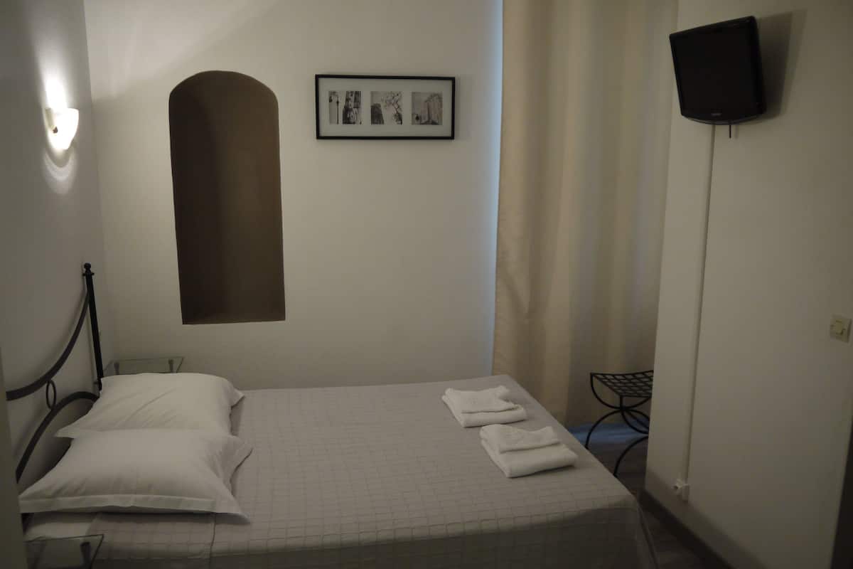A neatly made bed with pillows and a folded towel, a framed picture on the wall, and a television mounted on the wall.