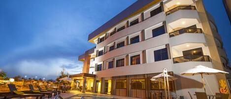 A multi-story hotel with a swimming pool, outdoor seating, and a guitar on the side.