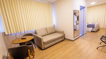A hotel room with a sofa, a small table, a chair, a bed, and a mirror.