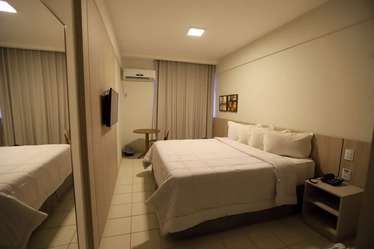A hotel room with a large bed, a bedside table with a phone, and a small table with a lamp.