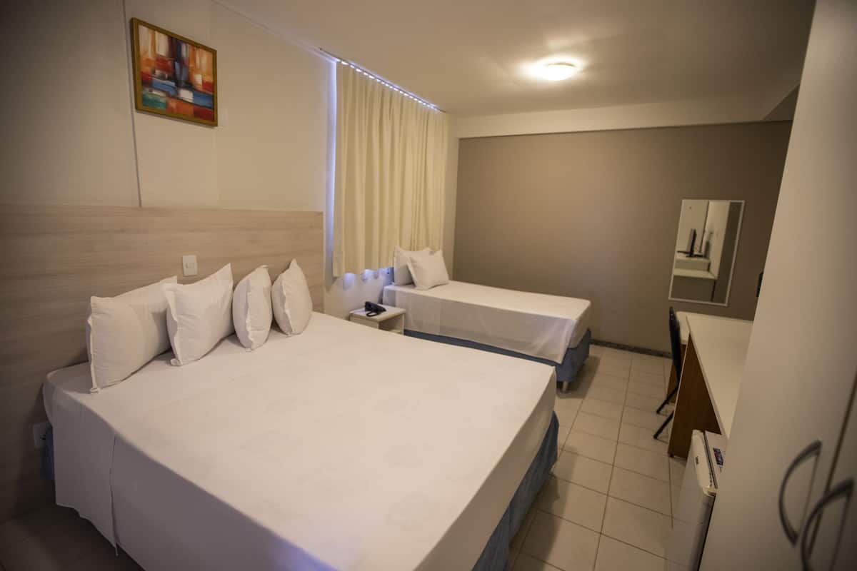 A hotel room with two beds, a small desk, a mirror, and a window with curtains.