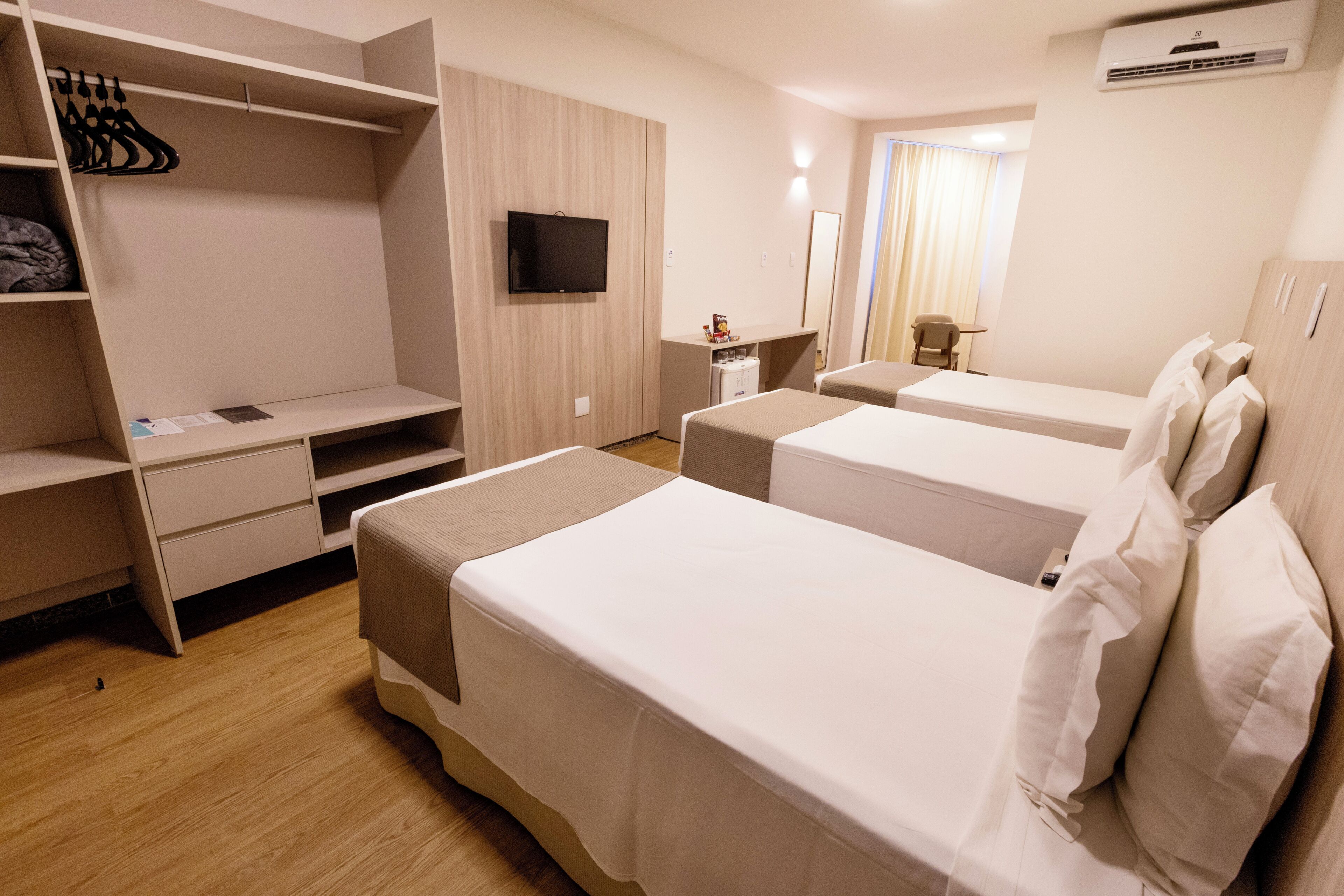 Habitación de hotel con dos camas, televisión, escritorio y armario.