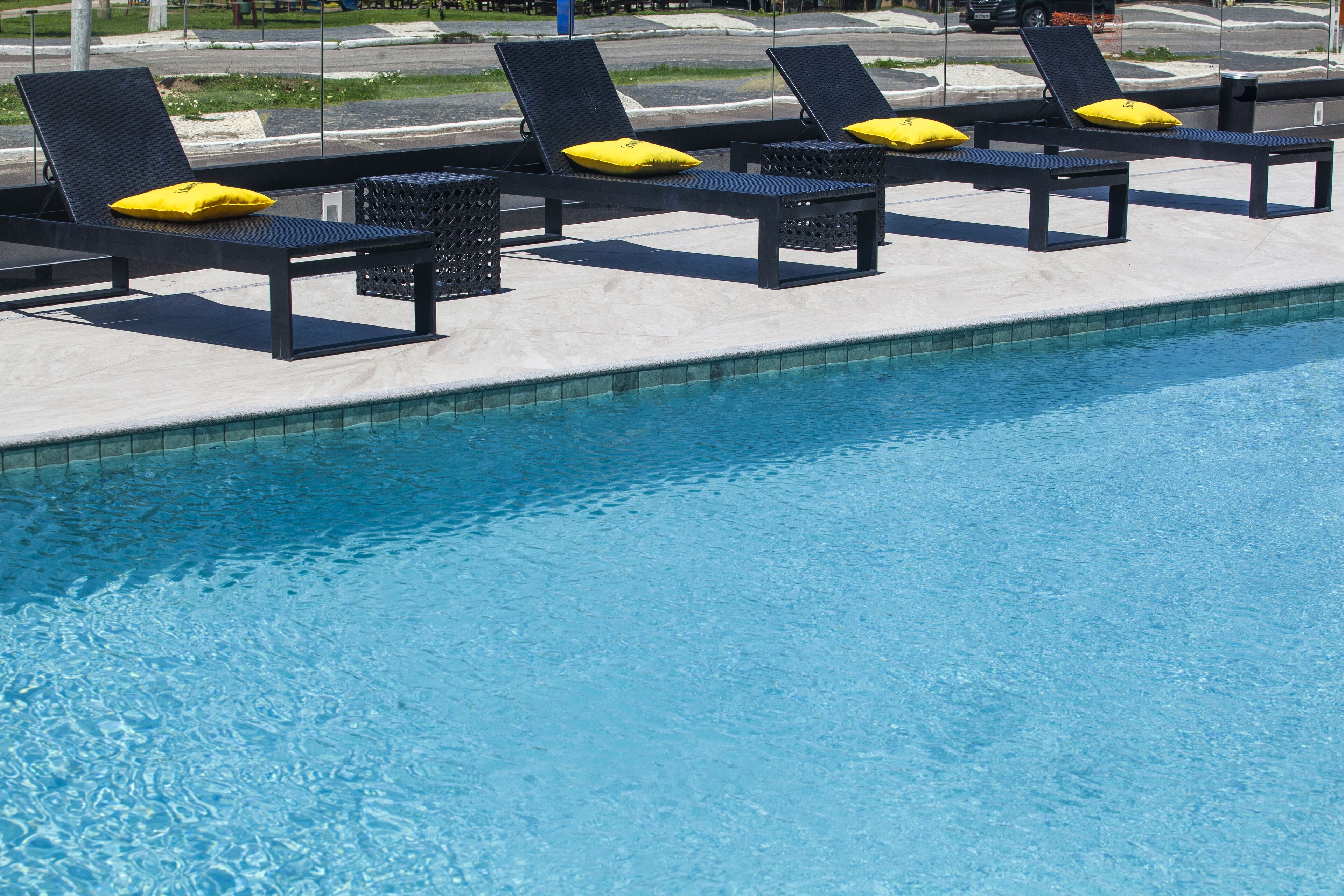 Un área junto a la piscina con sillones de descanso y cojines amarillos.