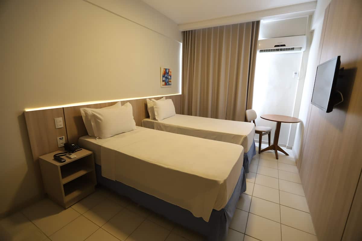 A hotel room with two beds, a bedside table with a phone, a small table with a chair, and a TV mounted on the wall.
