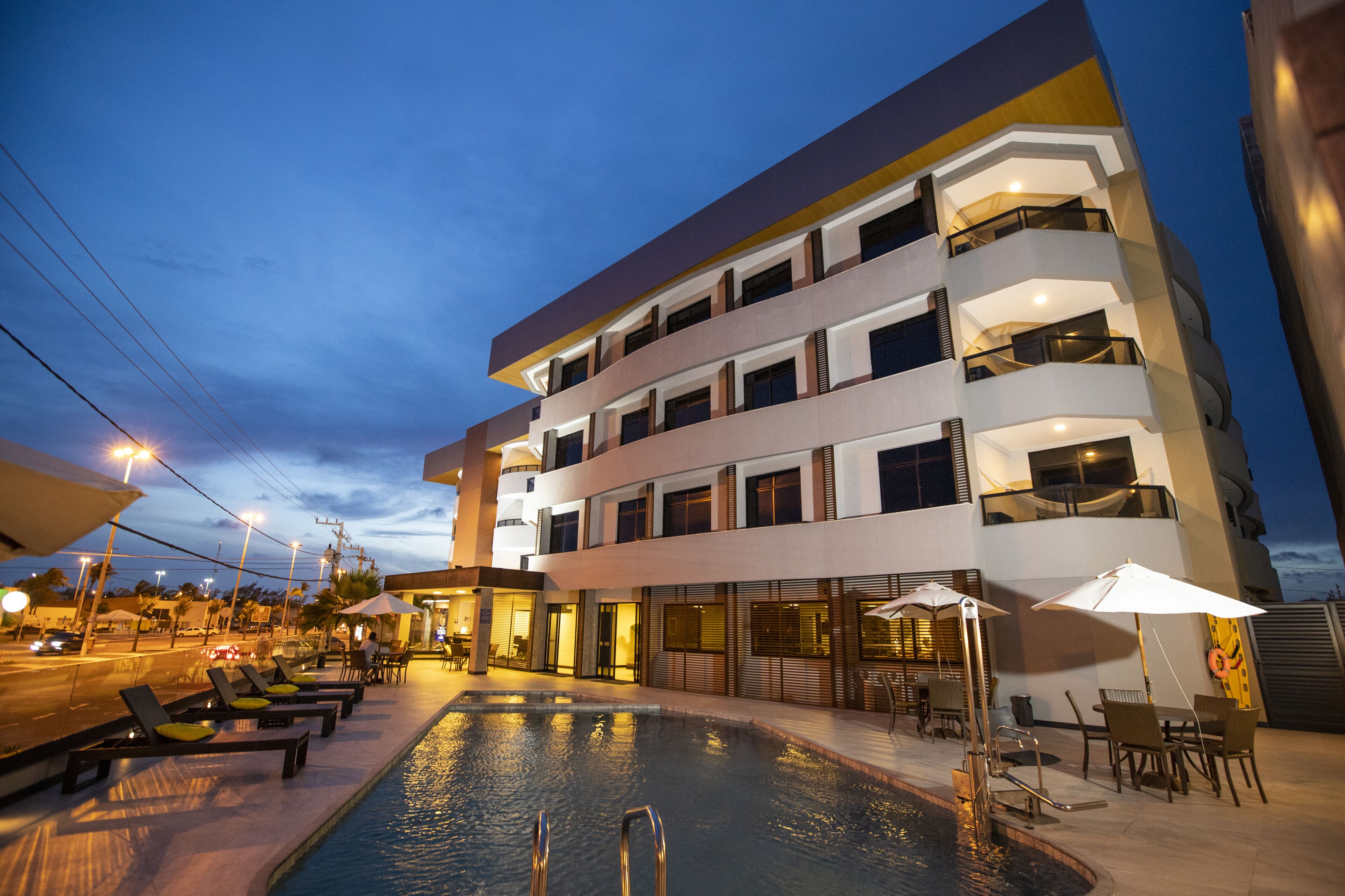 A modern hotel with a pool area, outdoor seating, and a well-lit entrance.