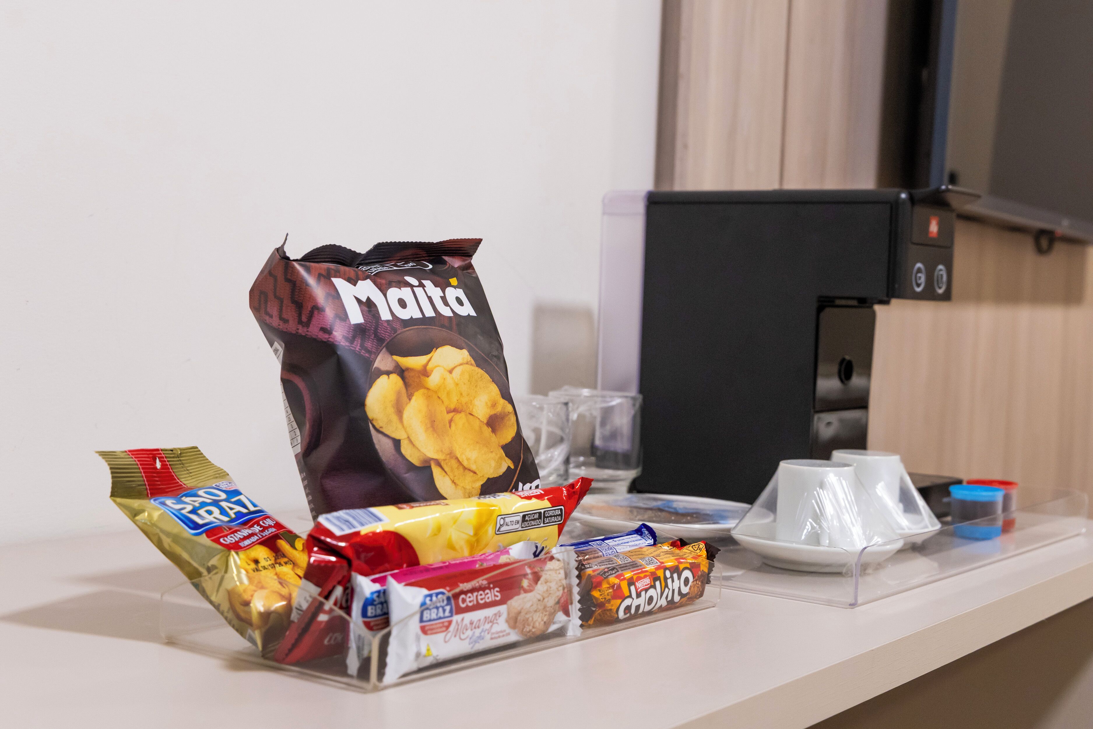 A kitchenette with a coffee machine, a bag of chips, cereal, and a packet of snacks.