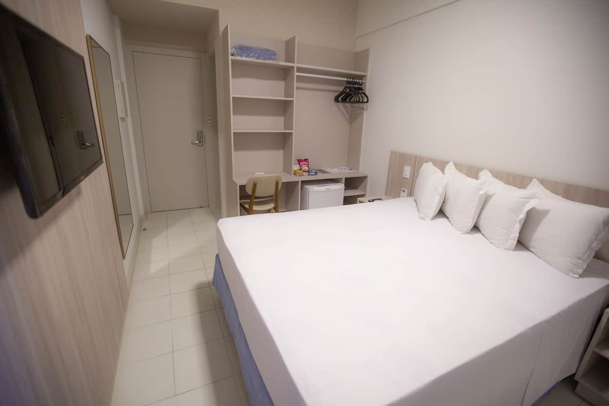 A hotel room with a large bed, a desk, and a wardrobe.