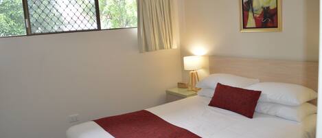 A hotel room with a bed, a nightstand, a lamp, and a window with curtains.