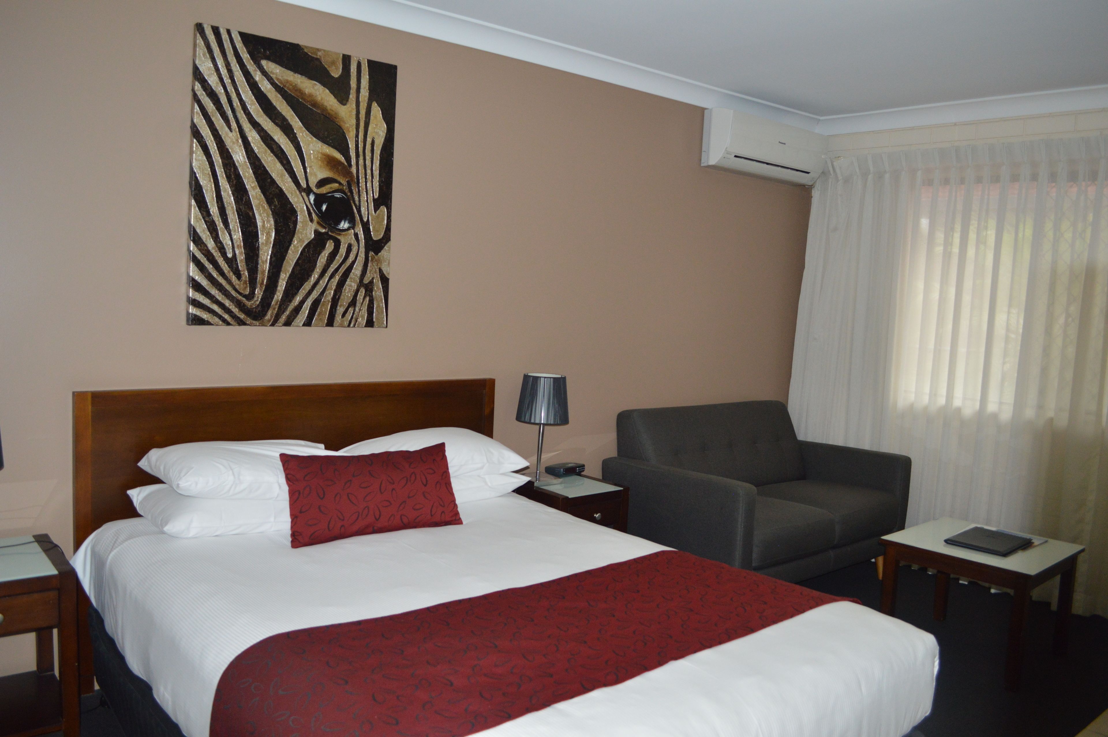 Habitación de hotel con una cama grande, un sillón gris, una mesita, una mesita de noche y una obra de arte con estampado de cebra en la pared.