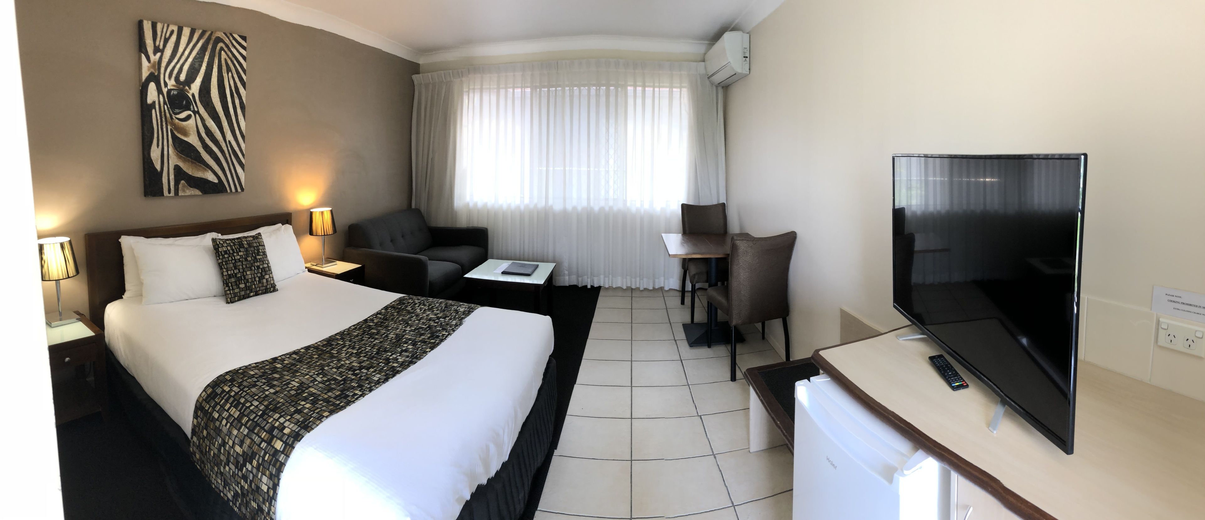 Habitación de hotel con una cama grande, un escritorio, una silla, un televisor y una ventana con cortinas.