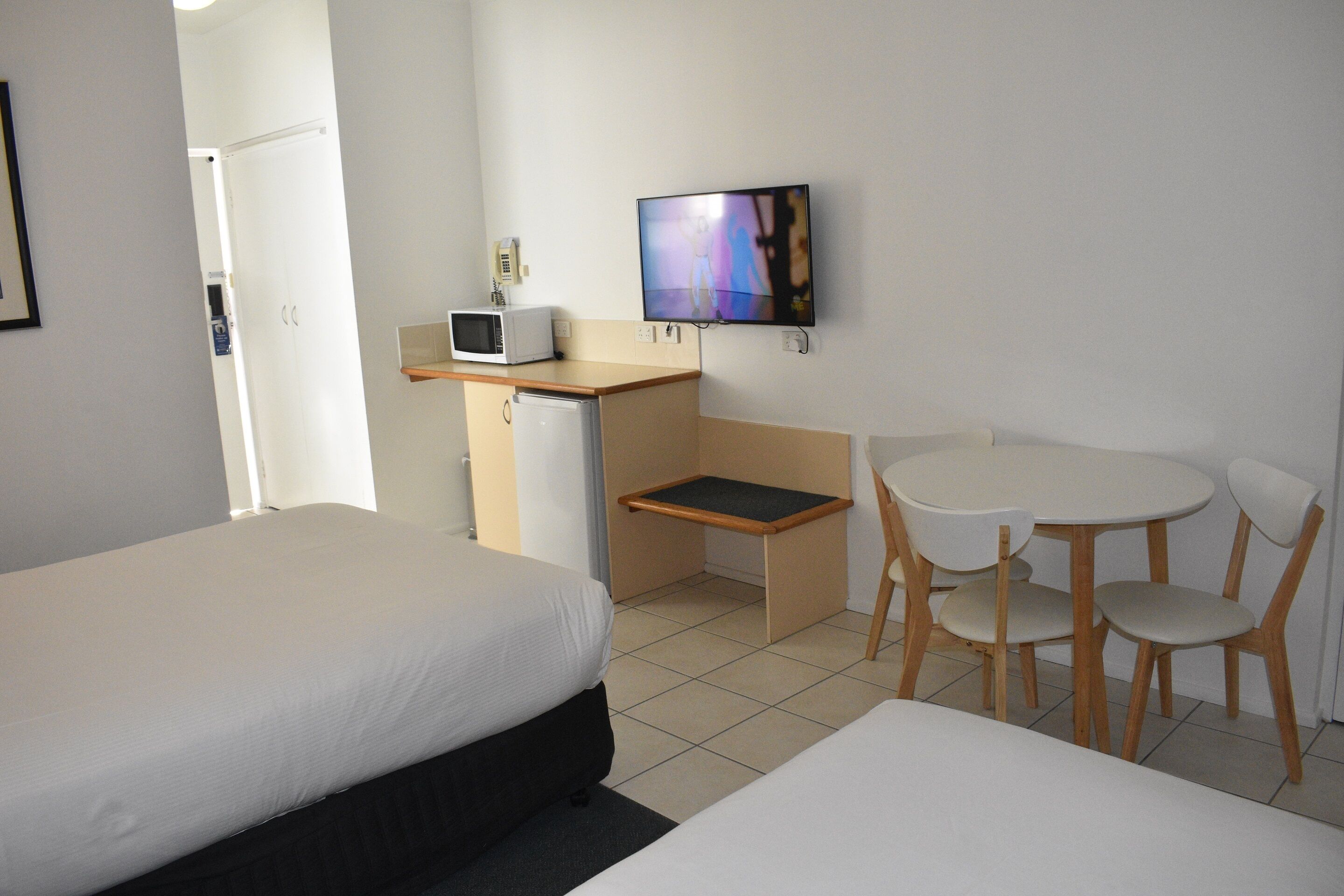 Habitación de hotel con dos camas, un escritorio con microondas, un televisor y una pequeña mesa con sillas.