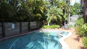 Una piscina con cubierta de madera y abundante vegetación alrededor.