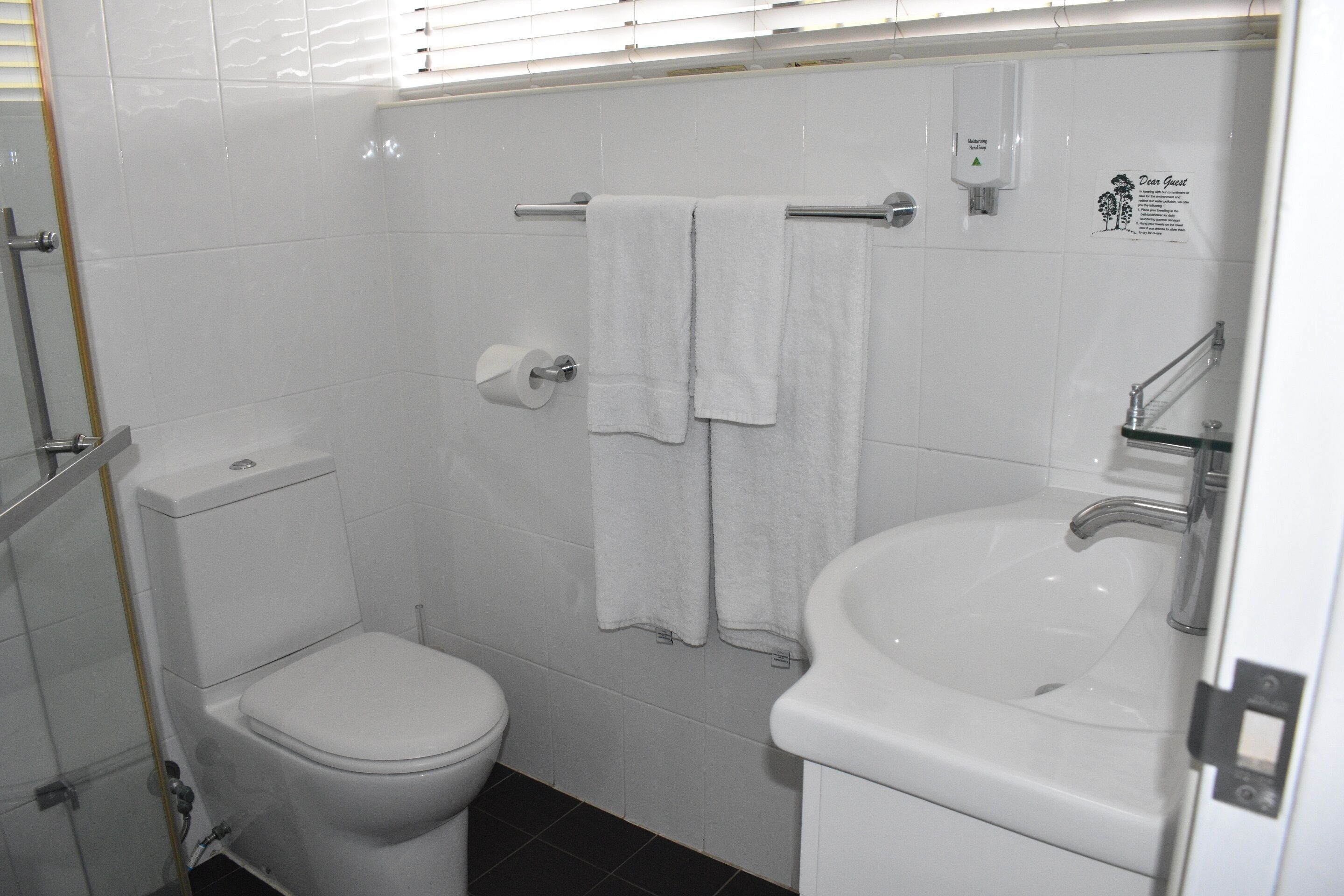 Un baño con inodoro, lavamanos y dos toallas colgadas en un perchero.