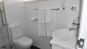 Un baño con inodoro, lavamanos y dos toallas colgadas en un perchero.