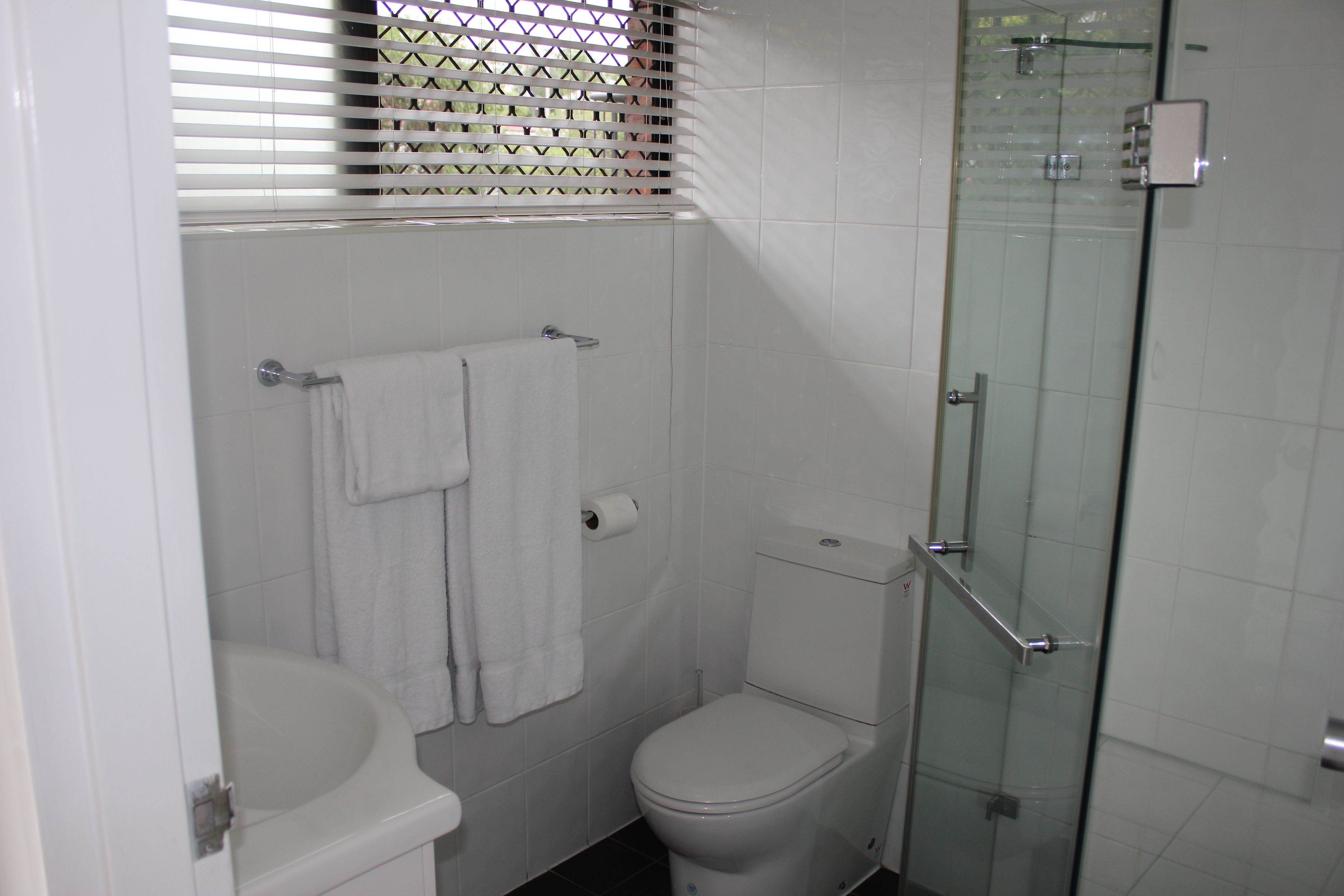 Een badkamer met toilet, een douche met glazen wand en een handdoekhouder.