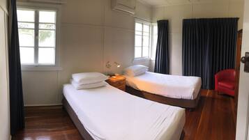 A hotel room with two single beds, a wooden floor, a red chair, and a window with curtains.