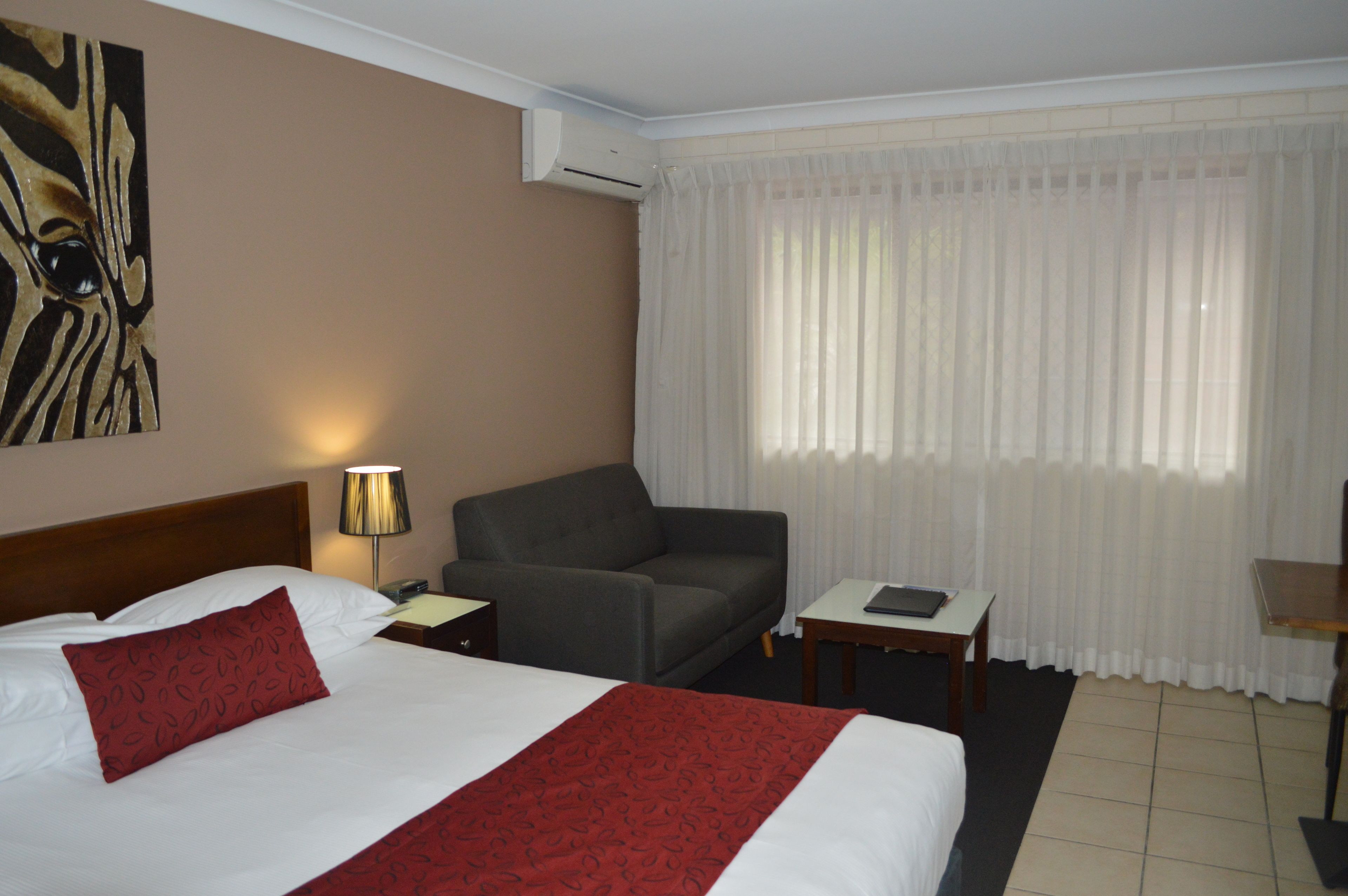 Habitación de hotel con cama, sofá, una mesita, lámpara y un cuadro en la pared.