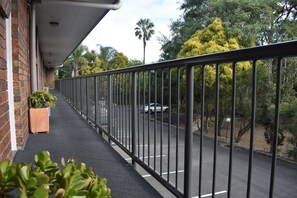 A covered outdoor balcony with a metal railing, potted plants, and a view of a road with cars and trees. - Best Western Ipswich (Ipswich)